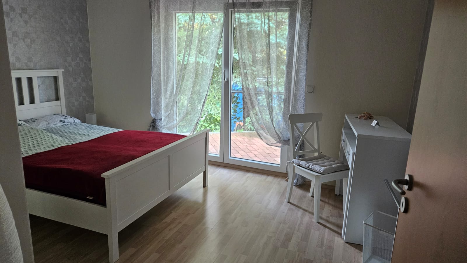 kleines Gästezimmer Helles Schlafzimmer mit einem Bett, Stuhl und Fenster zur Terrasse.